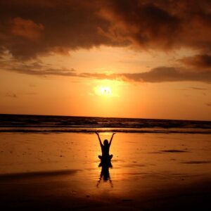 woman sat down facing sunrise on golden beach looking out at ocean